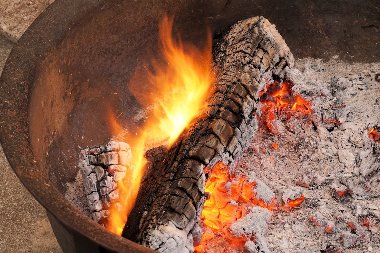 Detailed shot of burning logs in a fire pit with glowing embers and flames.